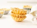 Montón de tartaletas de hojaldre listas para rellenar con crema pastelera.