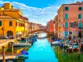 Colorate case affacciate su un canale con barche ormeggiate. Un ponte ad arco collega le due sponde. Un'immagine che ispira su cosa fare a Chioggia.
