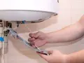 Main tenant vérifie son chauffe eau qui fait disjoncter. Il tient une pièce détachée avec des fils électriques.