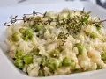 Kremowe risotto z groszkiem, posypane parmezanem i udekorowane gałązką tymianku. Pyszne danie, które zachwyca smakiem.