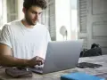 Mężczyzna w białej koszulce pisze na laptopie, przygotowując wniosek o urlop na poszukiwanie pracy.