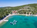 Malownicza zatoka z turkusową wodą, plażą i wodnym placem zabaw. W tle widać zabudowania i zielone wzgórza, idealne na camping Murter.