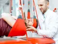 Fizjoterapeuta pomaga pacjentowi w terapii wiszącej, która może być jednym z zabiegów rehabilitacyjnych na kręgosłup lędźwiowy.