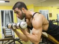 Man utför spider curls med hantlar på ett gym.