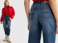 Kobieta w czerwonej kurtce i czerwonym T-shircie prezentuje modne **szerokie jeansy stylizacje**. Luźny krój i jasny denim tworzą swobodny look.
