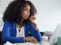 Frau hustet ins Taschentuch, während sie am Laptop arbeitet. Sie fragt sich, wie die Lohnfortzahlung bei einem Minijob auf Stundenbasis geregelt ist.