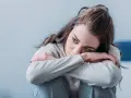 Smutna kobieta z dystymią tuli się do siebie, jej oczy wyrażają głęboki smutek i zmęczenie.