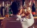 Mann wählt eine Flasche aus, in der reift Whisky in der Flasche nach. Viele Flaschen stehen im Regal.