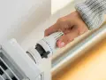 Dłoń reguluje termostat grzejnika, przygotowując się do wymiany termostatu.