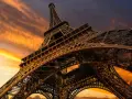 La Torre Eiffel, una icónica estructura de hierro forjado, se alza majestuosa contra un cielo anaranjado al atardecer.
