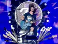 Dave Grohl z zespołem na scenie, szaleje z gitarą. Wokół niego mnóstwo gitar, a w tle wielkie logo i światła.
