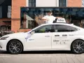 Mężczyzna w czapce z daszkiem stoi obok białego samochodu z logo Uber. To część floty Uber, gotowa do jazdy.