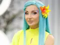Cleo w turkusowej peruce i neonowym żółtym topie, z barwnym makijażem i kwiatem we włosach, zapowiada nową piosenkę.