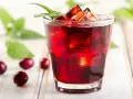 Orzeźwiający drink z żurawiną, lodem i listkiem mięty, otoczony kilkoma owocami żurawiny na drewnianym tle.