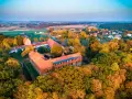 Zamek Bierzgłowski otoczony jesiennym lasem, z czerwonymi dachami i ceglanymi murami, w blasku zachodzącego słońca.