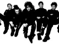 Les membres de The Cure, cinq silhouettes sombres aux coiffures distinctives, posent en groupe, l'air pensif.