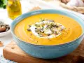 Vellutata di zucca cremosa, guarnita con panna, semi di zucca e timo, servita in una ciotola azzurra su un tagliere di legno.