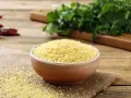 Cuenco de cuscús seco con perejil y chiles secos al fondo sobre una mesa de madera.