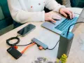 En person använder en laptop med en hubb ansluten till en telefon, extern hårddisk och powerbank. Hubben har usb 3.2-portar.