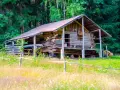 Drewniany bieszczady domek na odludziu, otoczony lasem i łąką. Wygląda jak miejsce na spokojny wypoczynek z dala od cywilizacji.
