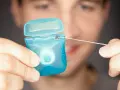 Mężczyzna trzyma niebieskie pudełko z nicią dentystyczną (floss).
