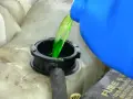 Green antifreeze is poured from a blue jug into a car's coolant reservoir. This raises the question: does antifreeze expire?