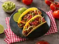 Dwa pyszne tacos z wołowiną, pomidorami, cebulą i serem, podane z limonką i guacamole.