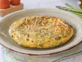 Tortilla de esparragos dorada y esponjosa, con trozos verdes de espárragos integrados en el huevo.