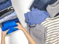 Ręce składają niebieski T-shirt, by pokazać, jak składać t shirty żeby się nie pogniotły. Obok leżą dżinsy i inne koszulki.