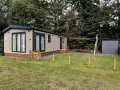 Nowoczesny dom holenderski z drewnianym płotkiem i zielonym trawnikiem, otoczony drzewami.