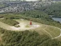 Luftaufnahme der Halde Rheinpreußen mit rotem Geleucht, umgeben von Wald und einem See.
