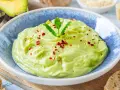 Cremige Avocado-Creme, garniert mit Minze, Sesam und Chiliflocken, serviert in einer blauen Schüssel. Perfekt als Dip oder Brotaufstrich.