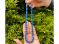 Collana di cianite blu, con perle luminose che catturano la luce, tenuta tra le mani su uno sfondo verde.