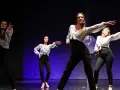 Kobiety w białych koszulach i czarnych spodniach tańczą na scenie. Pokazują, jak tańczyć solo na dyskotece, pewne siebie i pełne gracji.