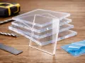 Stack of clear acrylic sheets, showcasing their plexiglass strength. Tools like a tape measure, drill bits, and ruler suggest a project in progress.