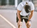 Atleta esausto con la testa china, mani sulle ginocchia, forse uno dei sintomi di overtraining.
