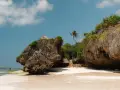 Plaża na Zanzibarze w maju. Skaliste klify, tropikalna roślinność i chatka z trawy. W oddali widać samotną postać.