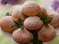 Stos puszystych pączków z piekarnika, oprószonych cukrem pudrem, ozdobiony listkami mięty.