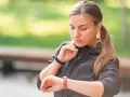 Kobieta w sportowej kurtce sprawdza na zegarku swój niski puls po treningu.