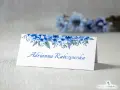 Eleganckie winietki dla usługodawców z motywem niebieskich kwiatów. Na białej kartce widnieje imię i nazwisko "Adrianna Rabczewska".