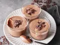 Drei Gläser mit luftiger Schokoladenmousse, garniert mit Schokostückchen. Ein Löffel zeigt die cremige Konsistenz dieses rezept mousse au chocolat ohne ei.