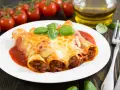 Cannelloni kontra naleśniki z mięsem: zapieczone w sosie pomidorowym i serze, ozdobione bazylią. Obok pomidorki i oliwa.