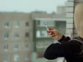 Kobieta z blond włosami pali papierosa na balkonie, zastanawiając się, czy w hotelach można palić na balkonie.