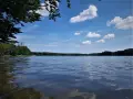 Spokojne jezioro Partęczyny z łagodnymi falami odbijającymi błękitne niebo i białe chmury. Lasy otaczają taflę wody.