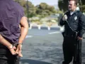 Mężczyzna w kajdankach, stojący tyłem do widza, podczas gdy policjant w mundurze obserwuje go. Powody zatrzymania na 48 godzin mogą być różne.