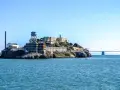 Słynne więzienie Alcatraz na skalistej wyspie, z charakterystyczną wieżą ciśnień i mostem w tle.