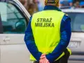 Strażnik miejski w kamizelce odblaskowej stoi obok samochodu.