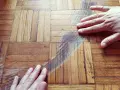 Mani sul parquet rovinato, mostrando i graffi e le macchie. Si valuta come pulire il parquet rovinato per riportarlo al suo antico splendore.