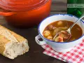Un reconfortante plato de patatas a la riojana, con chorizo y pimientos, servido en un cuenco blanco con borde azul, junto a una hogaza de pan rústico.