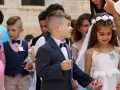 Chłopiec w eleganckim garniturze, z kokardką, wygląda jak z obrazka pin-up. Obok niego dziewczynka w białej sukience.